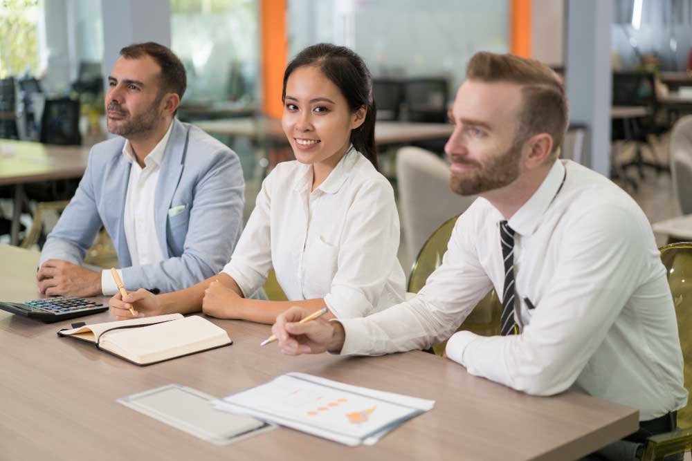 Business professionals listening attentively and taking notes during a strategy meeting, representing expert financial planning and transaction support through M&A Advisory California services.