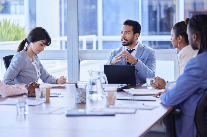 Business executives in a conference room discussing strategy around a table with laptops and documents, representing expert financial consulting and M&A Advisory Chicago services for mergers and acquisitions.