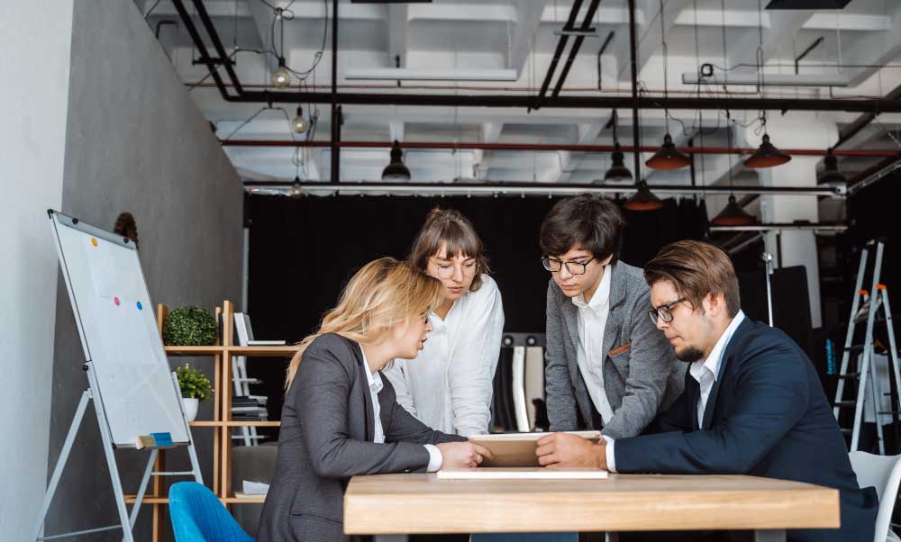 Business team collaborating around a table reviewing documents and discussing strategy in a modern office, representing professional financial planning and transaction support through M&A Advisory Florida services.