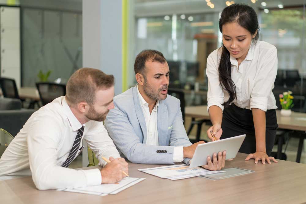 Business team collaborating around a tablet and reviewing financial reports in a modern office, representing strategic planning and professional transaction support through M&A Advisory Florida services.