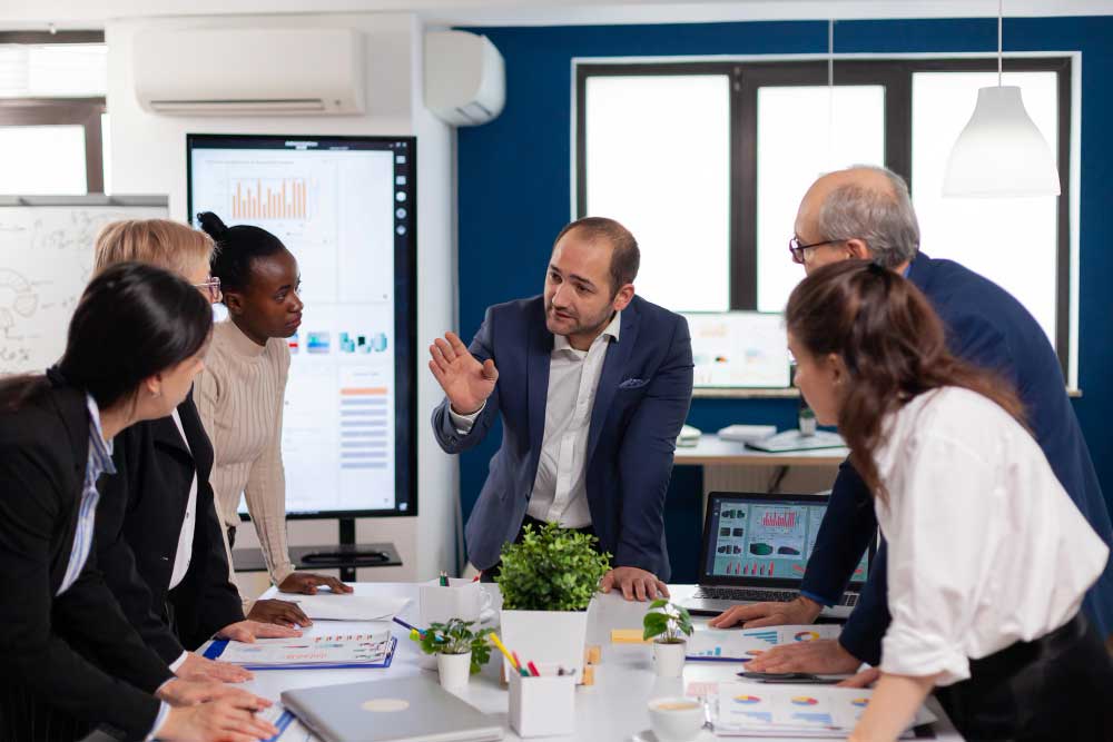 Business executives in a conference room discussing strategy around a table with laptops and documents, representing expert financial consulting and M&A Advisory Chicago services for mergers and acquisitions.